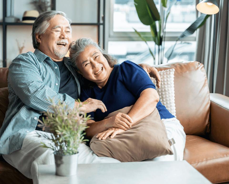 A middle aged couple laugh in an embrace as they sit on a couch in a modern living space